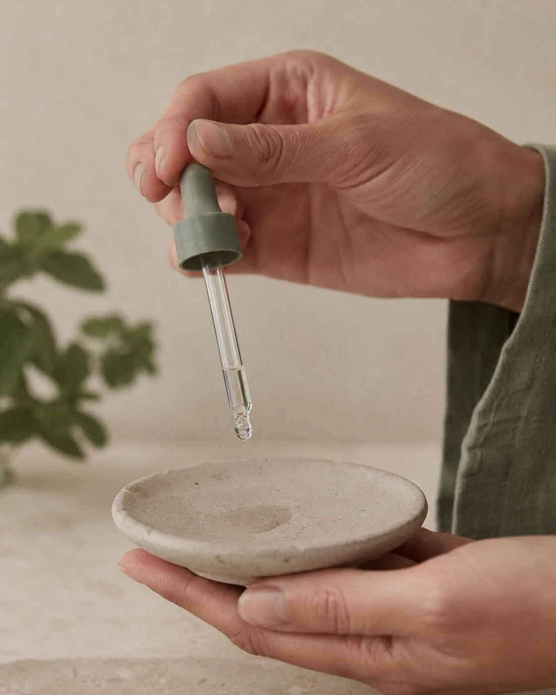 A woman receiving the CLINICCARE Cinderella facial: a glass serum dropper releases a single drop at her cheekbone, skin lit so it catches the light.